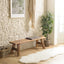 Reclaimed wood bench against a light stone wall with a small cushion and a potted plant, creating a warm, natural look.