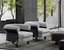 A pair of modern lounge chairs with plush grey upholstery and black curved armrests, set in a contemporary living space with floor-to-ceiling windows, greenery, and sleek black furnishings.